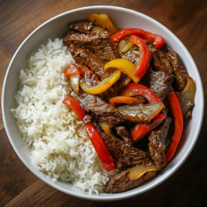 A bowl of garlic-ginger beef with sautéed bell peppers served alongside white rice.